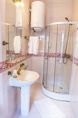 Simple bathroom featuring a rounded glass shower, pedestal sink, brass fixtures, white water heater and white towels