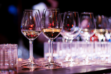 Elegant scene of wine being poured into glasses aligned in a row, showcasing the rich colors and graceful flow of the liquid, set against a dark, warm background, ideal sophisticated dining settings