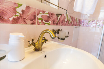 Brass faucet, pink floral tiles, and a clean white sink with matching accessories in thr bathroom. Home decor, interior design, and lifestyle imagery.