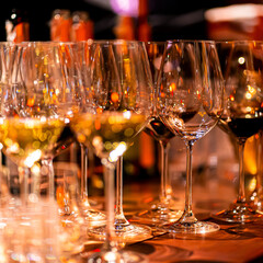 Elegant scene of wine being poured into glasses aligned in a row, showcasing the rich colors and graceful flow of the liquid, set against a dark, warm background, ideal sophisticated dining settings