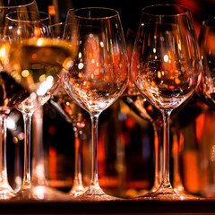 Elegant scene of wine being poured into glasses aligned in a row, showcasing the rich colors and graceful flow of the liquid, set against a dark, warm background, ideal sophisticated dining settings