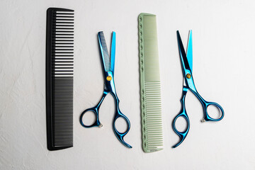 Hairdressing tools including black comb, green comb, and blue scissors arranged on a textured surface, showcasing essential equipment for professional hairstyling