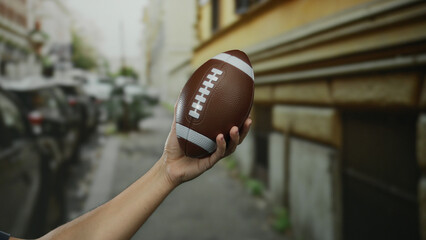 Man holding football while standing outdoors on a city street, captured in an urban setting with a...