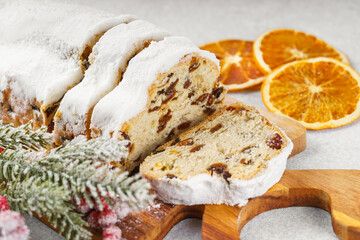 Traditional Christmas stollen, sweet fruit loaf sliced on wooden board, dusted with powdered sugar on white textured background. Spices, dried fruits and festive decorations create winter holiday mood