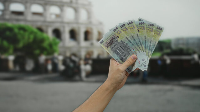 Male hand holding romanian banknotes near the roman coliseum, capturing a fusion of culture, travel, and finance in the heart of an ancient city street setting. - Powered by Adobe
