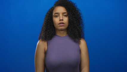 Hispanic woman wearing purple sleeveless top slumps bare shoulders in studio facing blue wall;...
