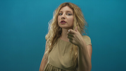 Fototapeta premium Woman extends hand forward showing forearm and open palm wearing beige dress in teal studio; invitation confidence.