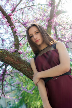 Young woman in a burgundy dress standing beside a tree with small pink blossoms