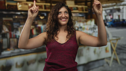 Woman pointing both index fingers upward with bare arms visible at a street market stall, smiling and eyes closed; celebration joy.