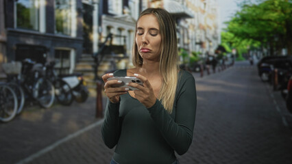 Woman holding smartphone with hand on cheek on a city street, looking down at the screen with a pensive pout; disappointment reflection.