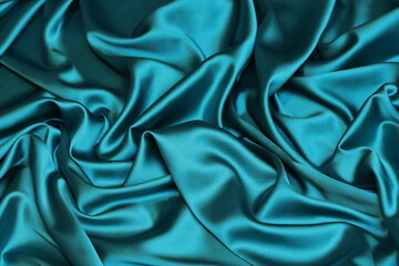 Fototapeta premium Close-up of soft, flowing turquoise blue Charmeuse satin texture. Ideal luxurious background for high-end fashion, beauty, or celebration themes.