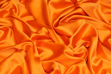 Close-up of soft, flowing orange Charmeuse satin texture. Ideal luxurious background for high-end fashion, beauty, or celebration themes.