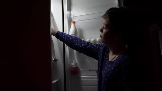 Child in pajamas opens refrigerator, examining contents with curiosity, camera pans to reveal items, showcasing a moment of discovery and decision-making in a cozy kitchen setting