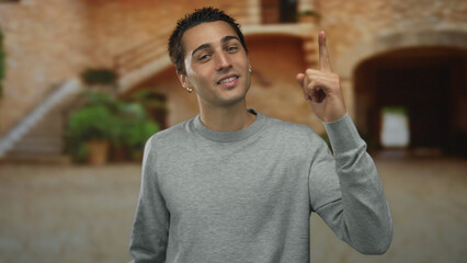 Young man smiling outdoors in old town showing thumbs up gesture while enjoying the scenic historic atmosphere.