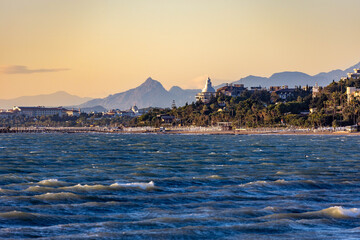Wavy blue sea with whitecaps under evening sun, viewed from the water towards a resort coastline...