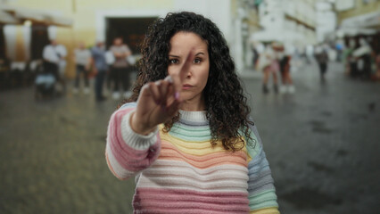 Fototapeta premium Woman in colorful sweater outdoors on street showing rejection with crossed arms and serious expression amid blurred urban background depicting disagreement