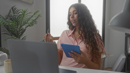 Woman seated at desk holding blue tablet and stylus while reading from screen in studio; concentration productivity.