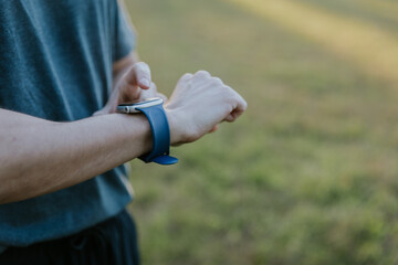 Man adjusting fitness tracker while standing in sunlit open air field