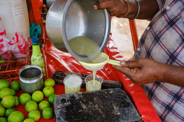 Indian street vendor pouring fresh sugarcane juice into glass at roadside stall with limes, highlighting traditional summer drink preparation and vibrant local market scene