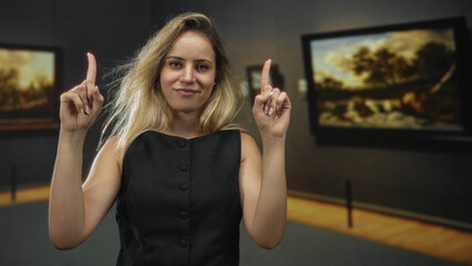 Woman pinches fingers near face while pointing index finger upward in museum building, hands...
