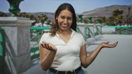 Fototapeta premium Woman showing open palms in a shrug gesture on a seaside promenade street with green balustrade and palm trees; playful curiosity.