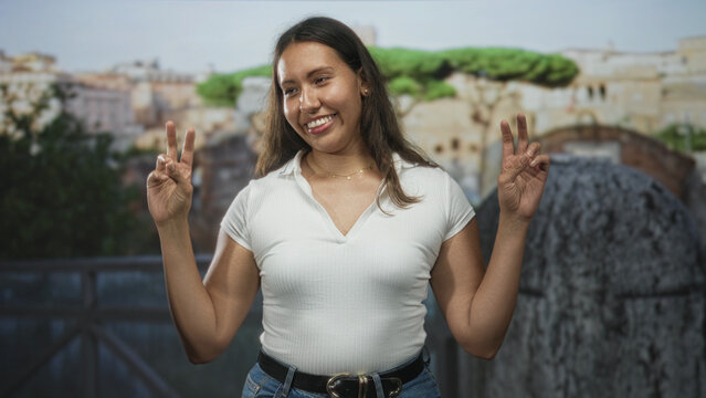 Woman wearing white top holds both hands in peace sign on roman ruins building terrace, smiling at camera; travel exploration joy. - Powered by Adobe
