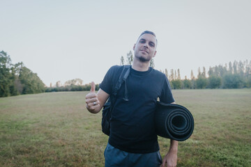 Man giving thumbs up after workout in open air park with exercise mat and backpack