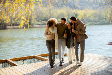Friends enjoying a sunny lakeside stroll in autumn with drinks in hand amidst nature's beauty