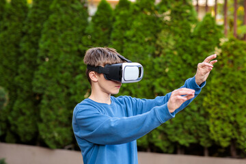 Young teenage boy wearing a virtual reality headset, reaching out and interacting with a digital world in an outdoor garden setting