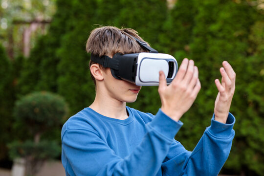 Concentrated young teenage boy wearing a virtual reality headset, reaching and interacting with an invisible digital world outdoors