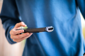 Close-up of a young person's hands holding a smartphone horizontally and typing or interacting with the screen, wearing a blue sweater