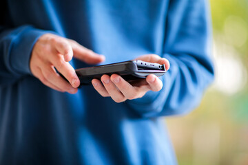 Close-up of a young person's hands holding a smartphone horizontally and typing or interacting with the screen, wearing a blue sweater