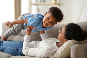 African american mother and son playing airplane on sofa at home lifestyle