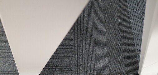 Minimalist geometric composition showing textured office carpet and angled white panels, creating a clean modern abstract design.