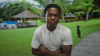 Man wearing eyeglasses and polo shirt with crossed bare arms standing in a resort pool area by a...
