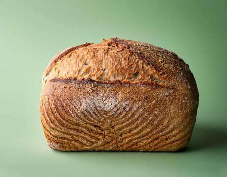 a dense spelt bread loaf with a crusty surface on a pastel green background