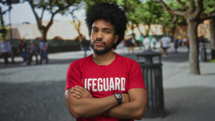 Lifeguard man with crossed arms in city outdoor setting expresses disapproval as people walk in the...
