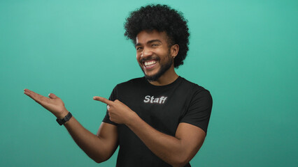 Smiling man in staff uniform points confidently at hand against vibrant green background, engaging...