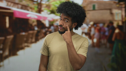Man pointing to eye while standing in a bustling outdoor market street in a city, surrounded by...