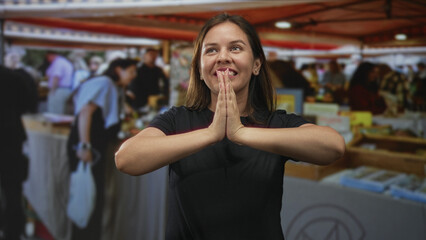 Woman pressing palms together at a bustling outdoor market stall in the city, looking upward; gratitude souvenir memory.