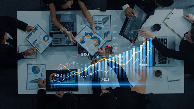 High-angle view of a business meeting featuring professionals discussing financial graphs and data analytics, showcasing teamwork and strategy development in a modern office environment. Scalp