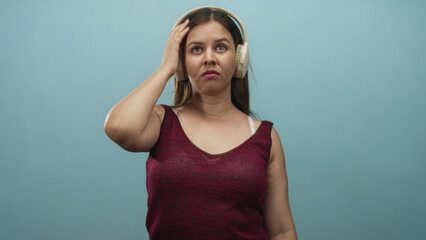 Woman adjusting over ear headphones with hand to ear in studio with teal wall; skepticism listening.