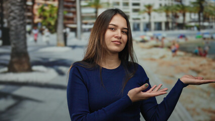 Hispanic woman standing on a seaside promenade extends her hands, embodying calm in an outdoor setting, with palm trees and beachgoers creating a lively background.