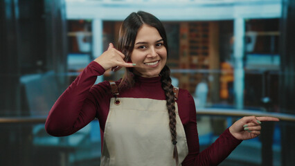 Waitress in apron making phone gesture indoors in a hotel setting showing hospitality and customer...