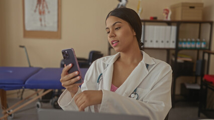 Woman doctor holds smartphone in clinic with stethoscope draped around neck and blue examination...
