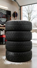 Stack of four winter tires lightly dusted with snow in a home garage. Seasonal car maintenance and preparation for cold weather driving.