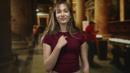 Woman with hand on chest, eyes closed in church building among candles and columns, wearing maroon shirt; devotion serenity.
