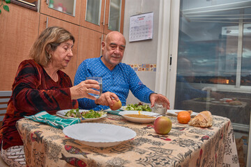An elderly couple shares a home-cooked meal in their dining room with affectionate gestures and a...