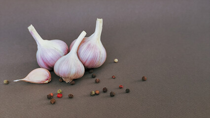 Heads of garlic on a gray background, scattered peppercorns, top view with space for text