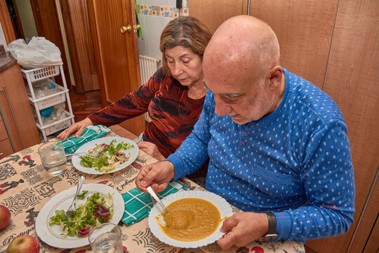An elderly couple shares a home-cooked meal in their dining room with affectionate gestures and a sense of connection that reflect lasting love.